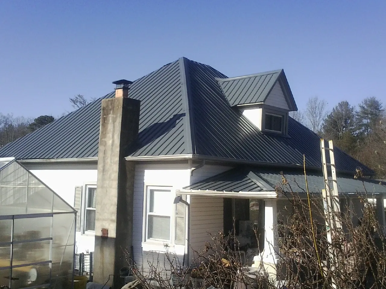 Dark blue standing seam metal roof on a white farmhouse with dormer — Slate & Tile Roof Repair by Roofing Brothers in Orovada
