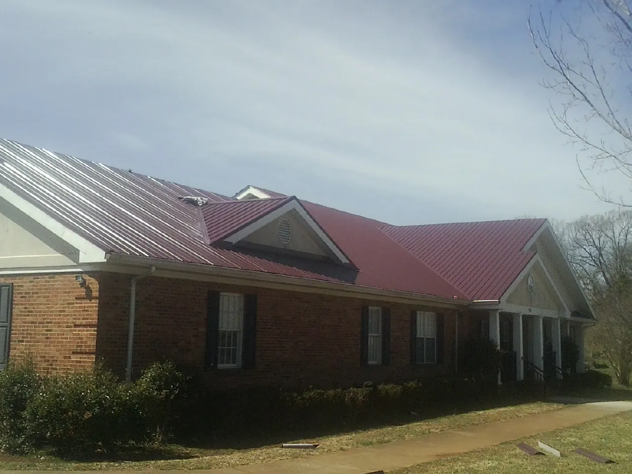Red metal roof with gabled entries on a long brick building, from a Hail Damage Roof Repair job in Orovada
