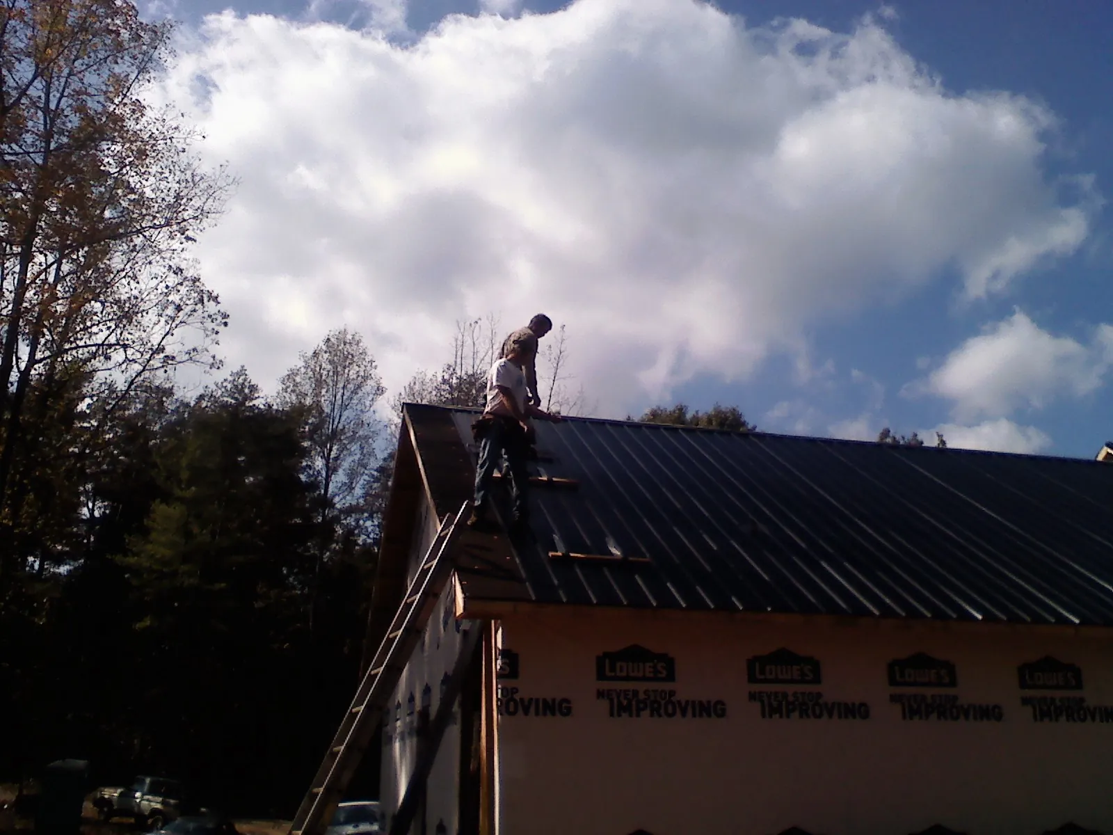 Roofer fastening dark metal panels high against a cloudy sky, from a Roof Inspection job in Orovada